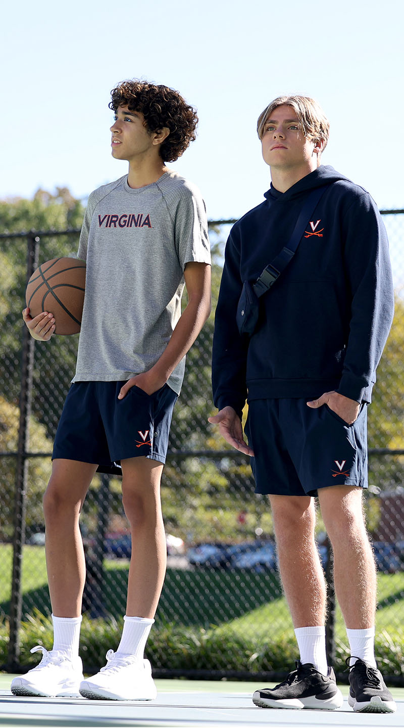 From the lululemon meets UVA collection two students on a basketball court, one wearing a gray tee shirt, the other a blue hoodie, both over blue shorts.