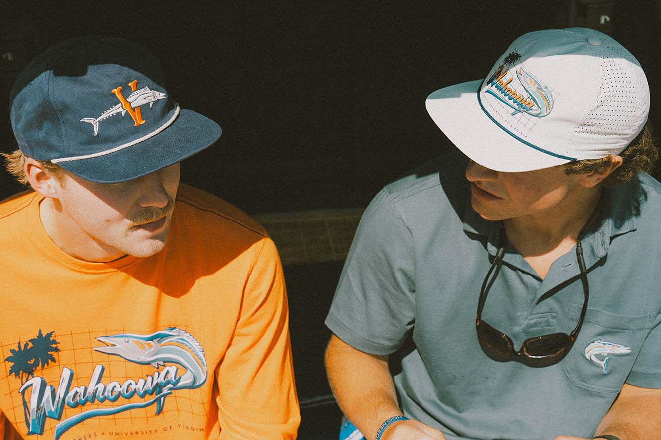 A blue Howler Bros. UVA hat and orange longsleeve shirt and a white hat and blue polo shirt