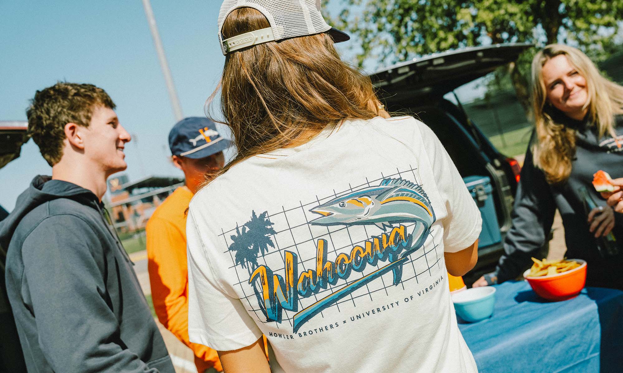 A tailgate party where every guest is wearing Howler Bros. UVA gear, featuring the back of a Wahoowa tee shirt